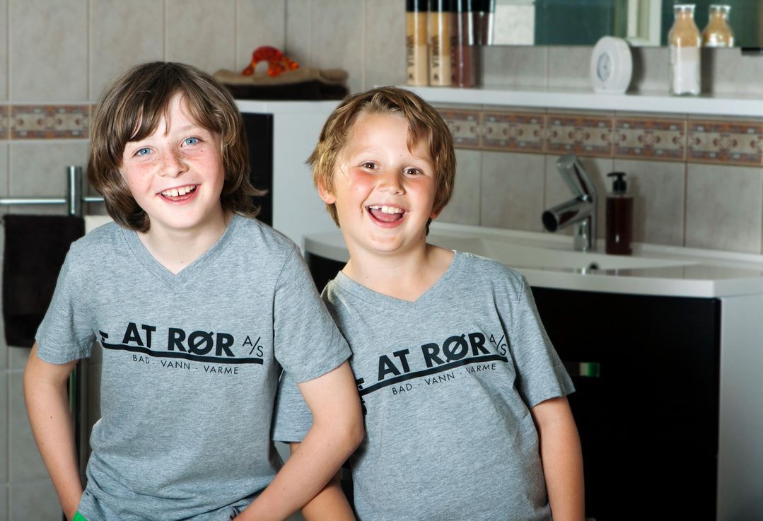 2 blide gutter med A&T Rør AS skjorte i et baderom